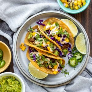 Grey plate with three vegan chorizo tacos surrounded by bowls of taco ingredients.