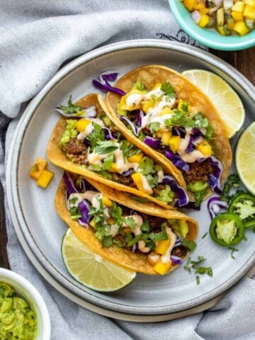 Grey plate with three vegan chorizo tacos surrounded by bowls of taco ingredients.