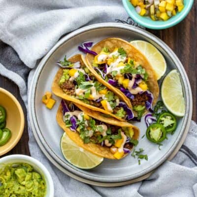 Grey plate with three vegan chorizo tacos surrounded by bowls of taco ingredients