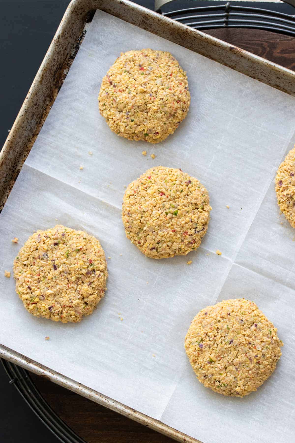 Uncooked falafel burger patties on a parchment lined baking sheet.