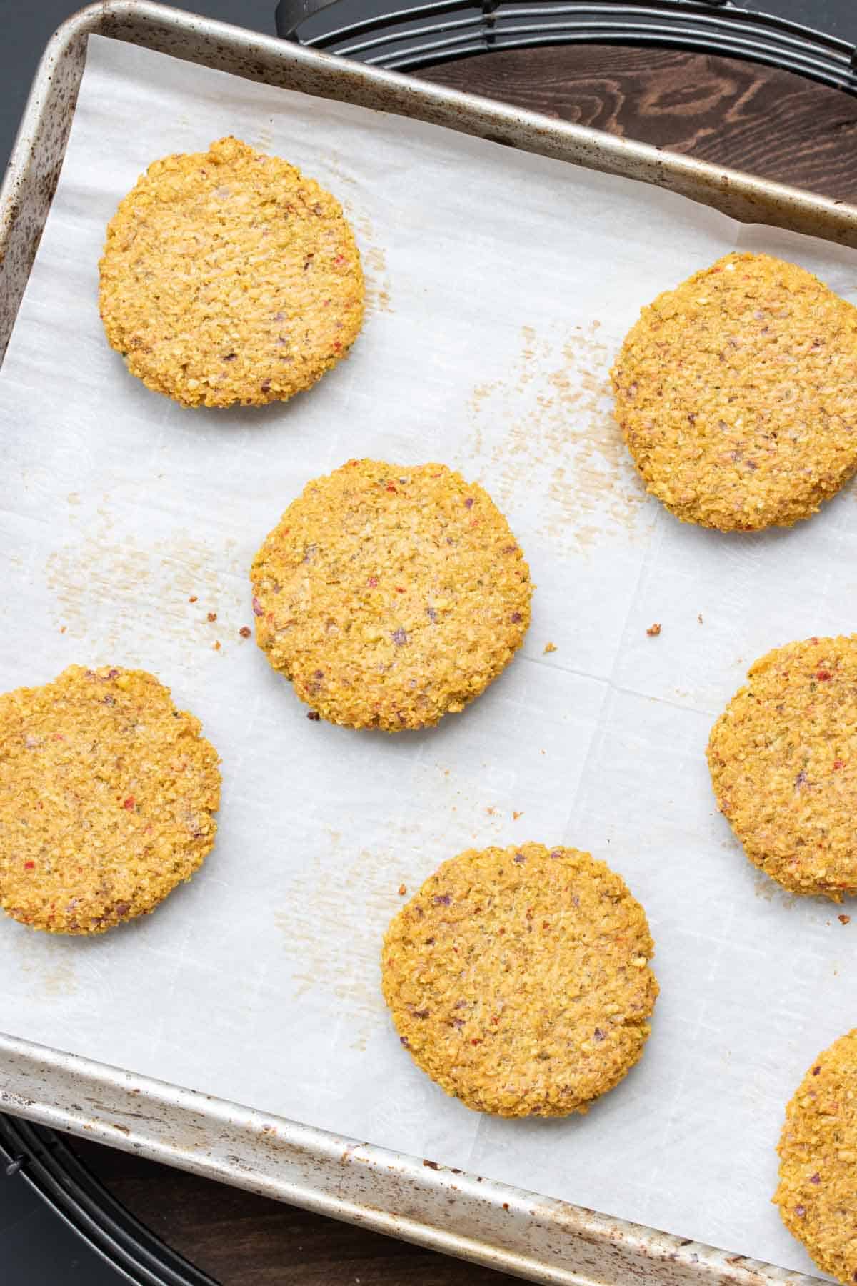 A parchment lined baking sheet with baked falafel burgers on it.