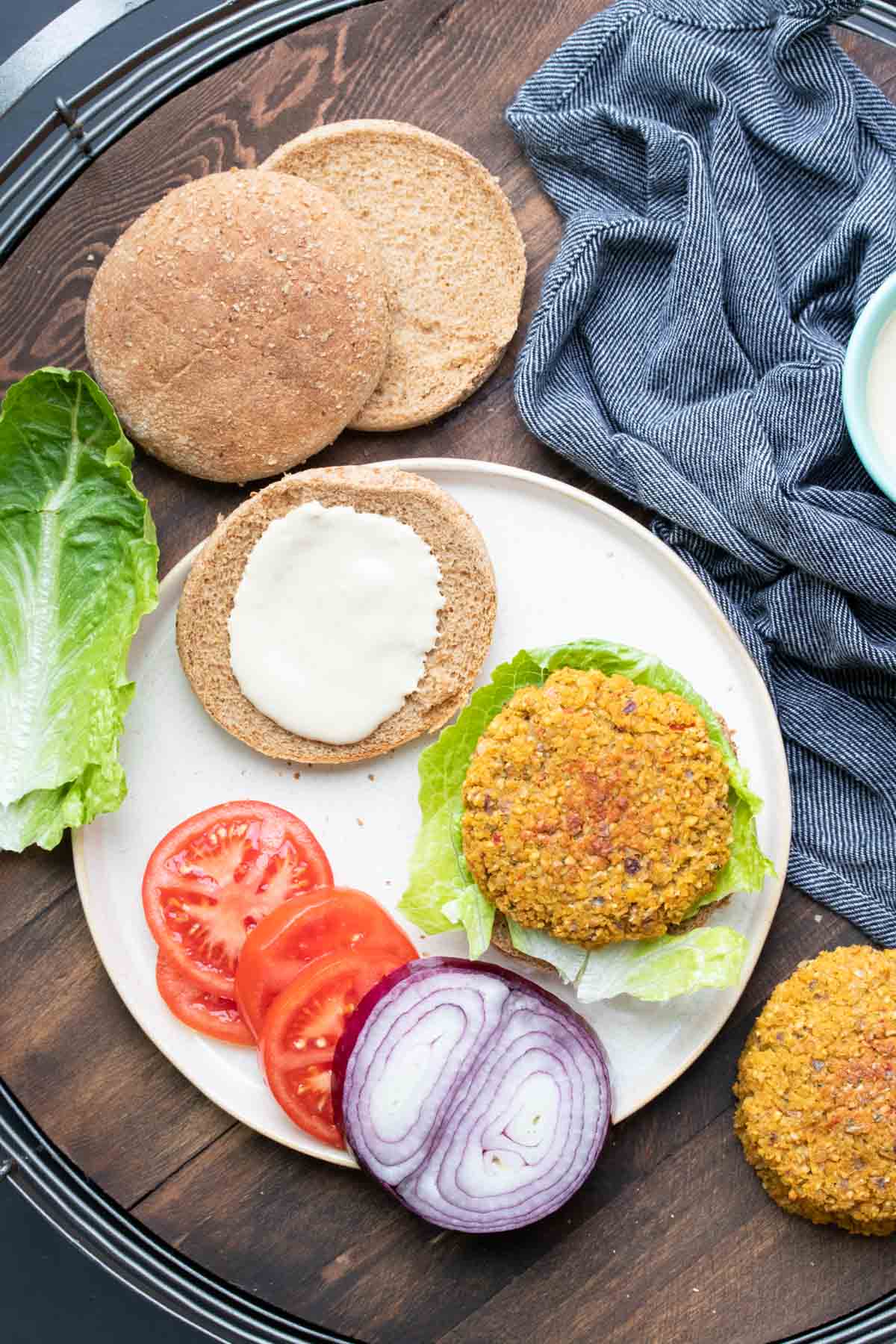 White plate with an open faced falafel burger on a bun surrounded by toppings.