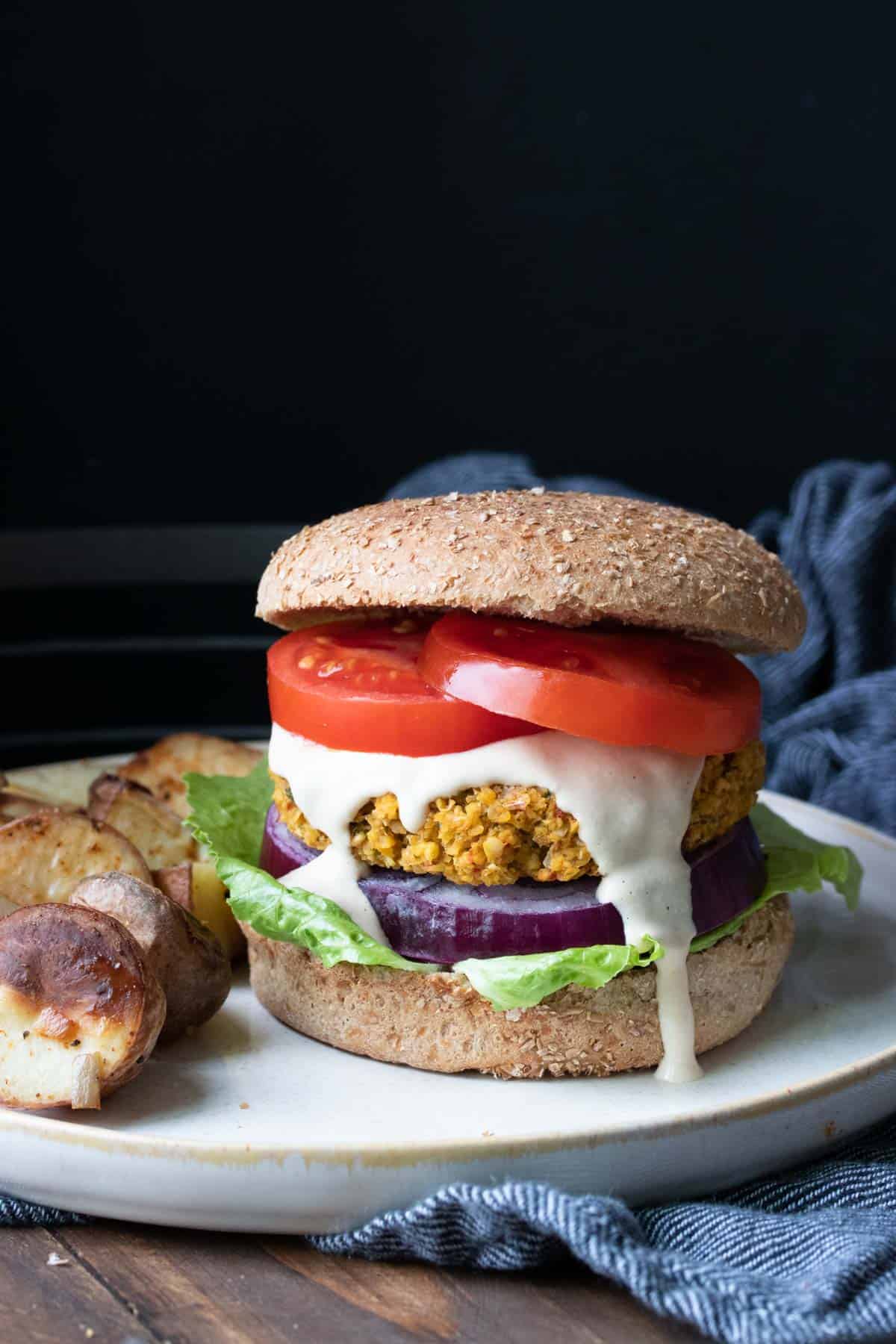 A falafel burger topped with lettuce, tomato, red onion and sauce on a white plate.