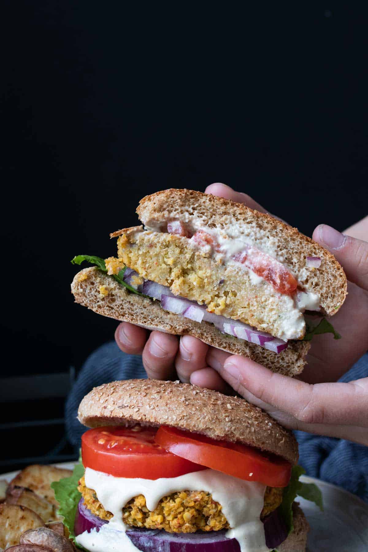 Hands holding half a falafel burger over a whole burger.