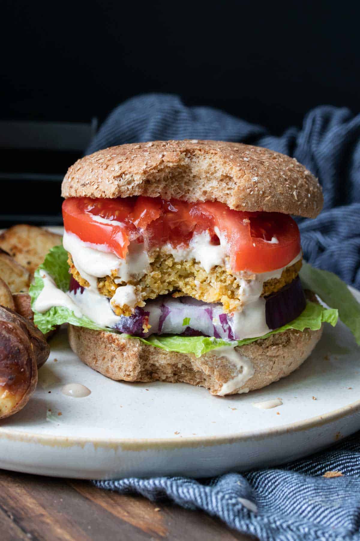 Falafel burger with lettuce, tomato and red onion and a bite out of the front.