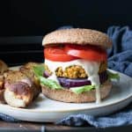 White plate with a falafel burger dripping with sauce next to roasted potatoes.