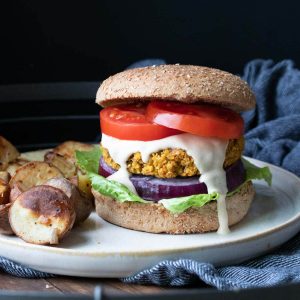 White plate with a falafel burger dripping with sauce next to roasted potatoes.