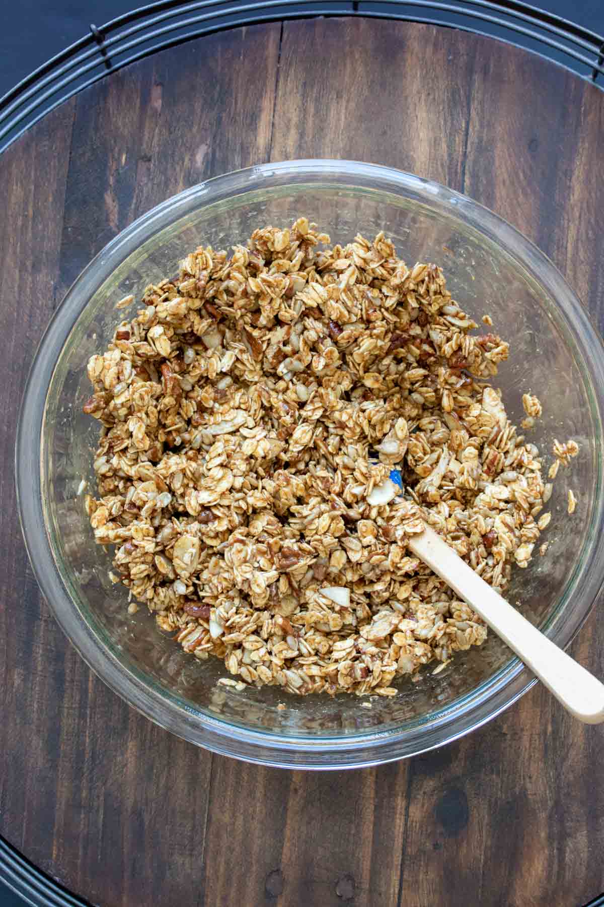 Spatula mixing ingredients for homemade granola in a glass bowl