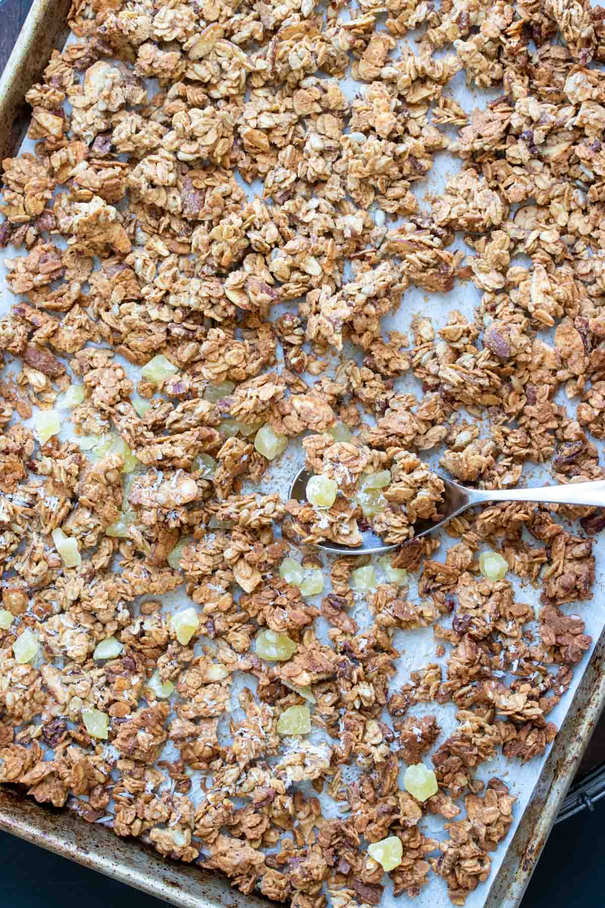 Spoon scooping baked granola from a pan