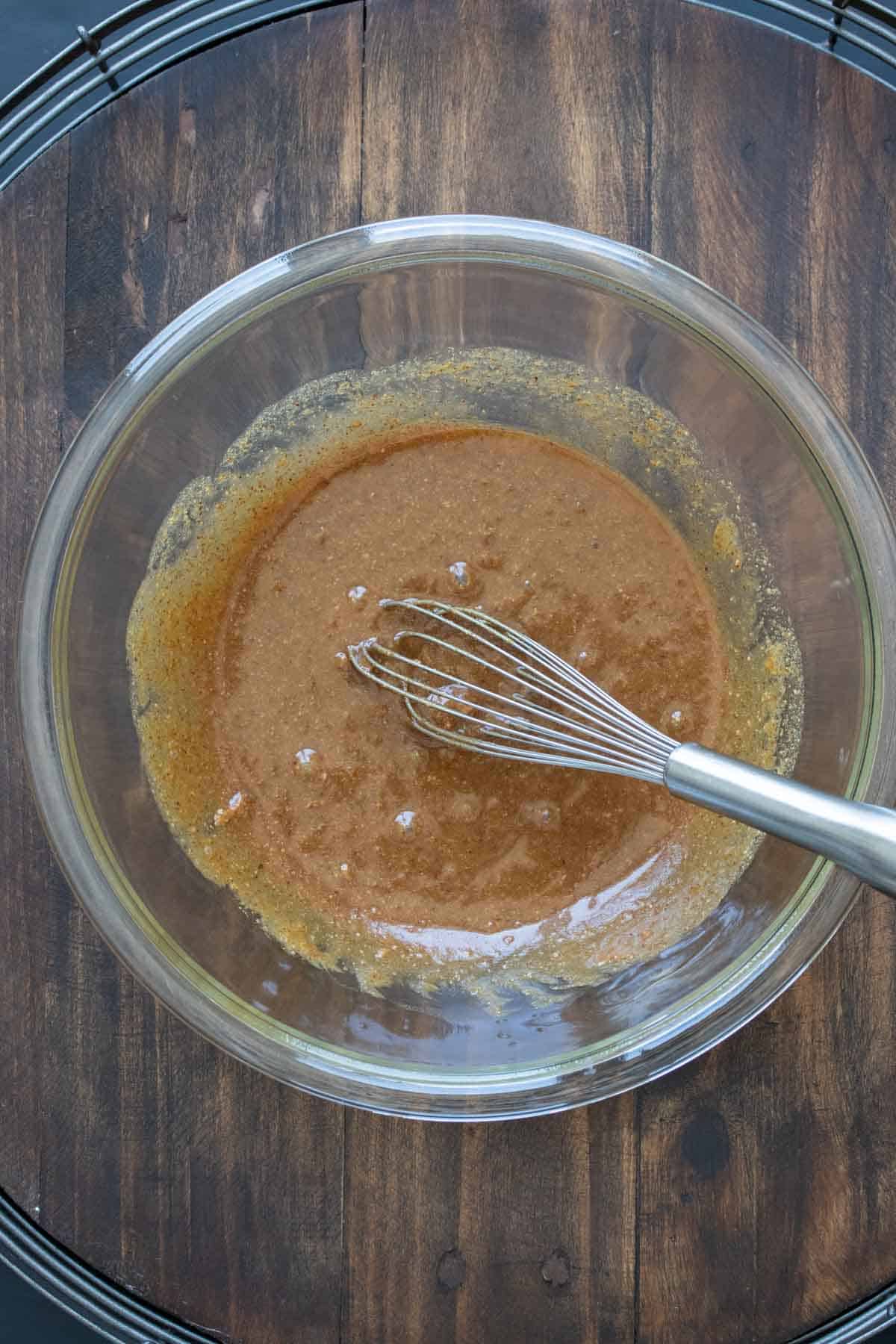 Whisk mixing a syrupy brown liquid in a glass bowl