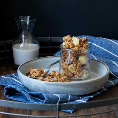 Granola in a glass jar sitting on a grey plate in front of a glass of milk