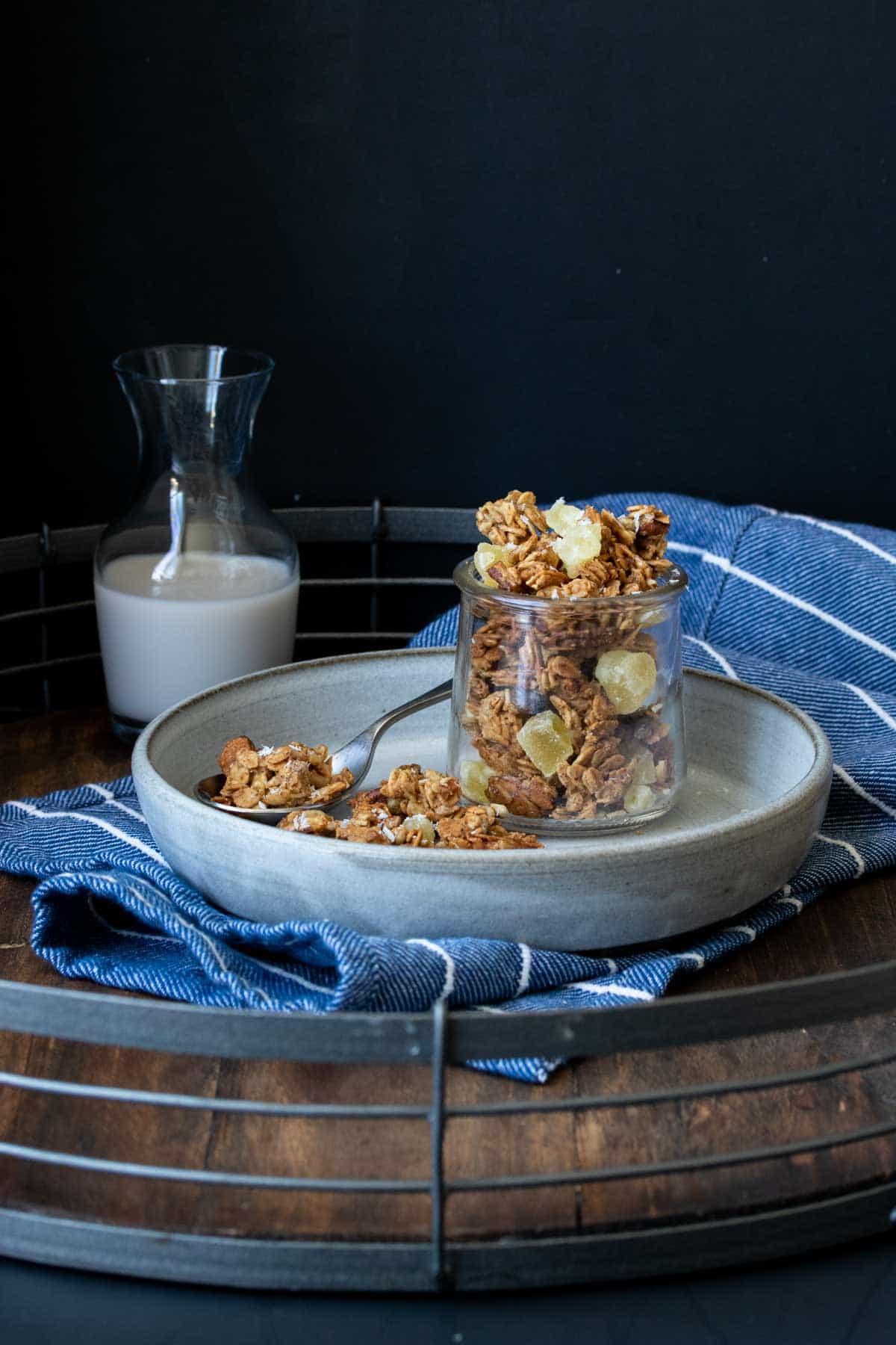 Granola in a glass jar sitting on a grey plate in front of a glass of milk