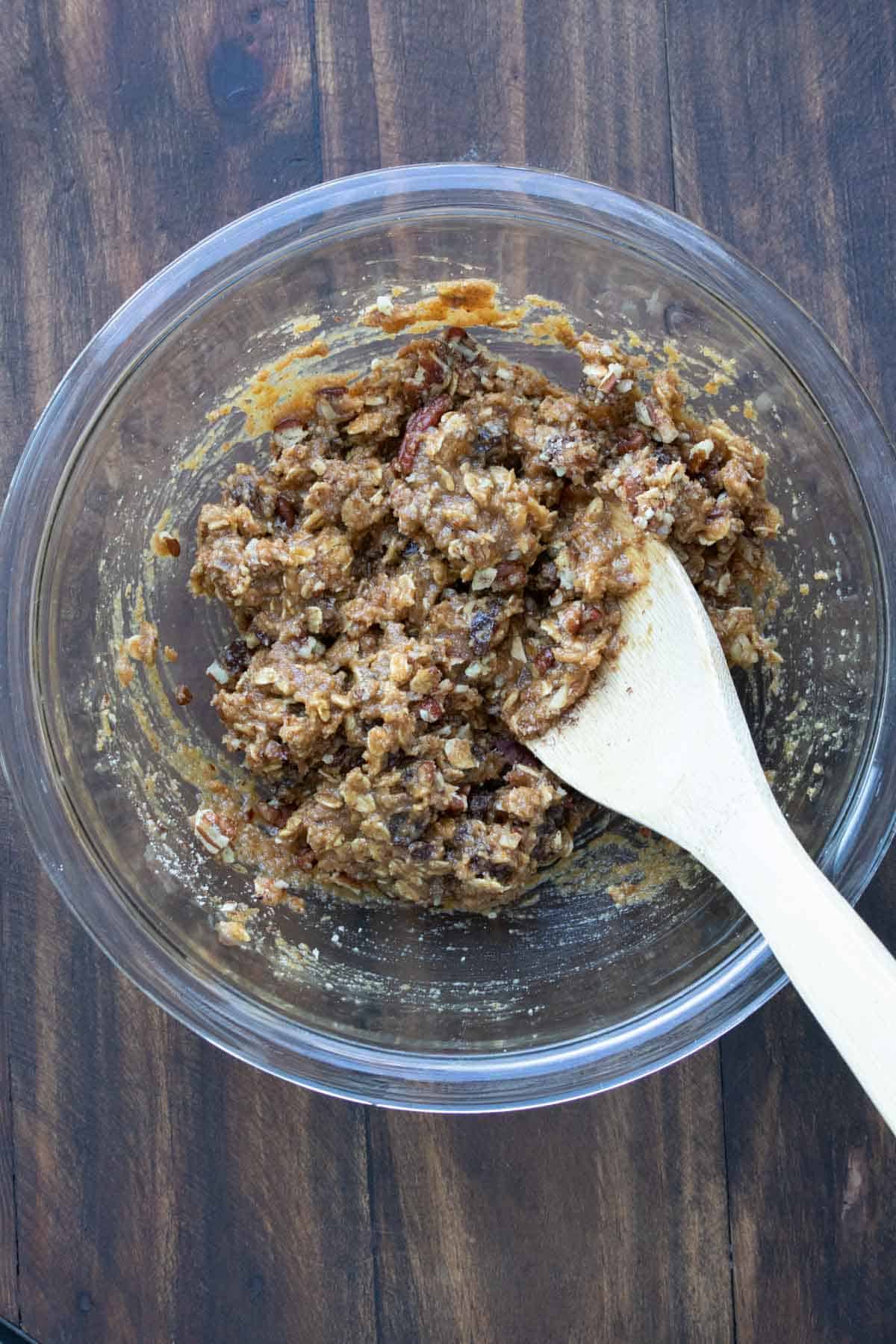 Wooden spoon mixing oatmeal raisin cookie dough in a glass bowl