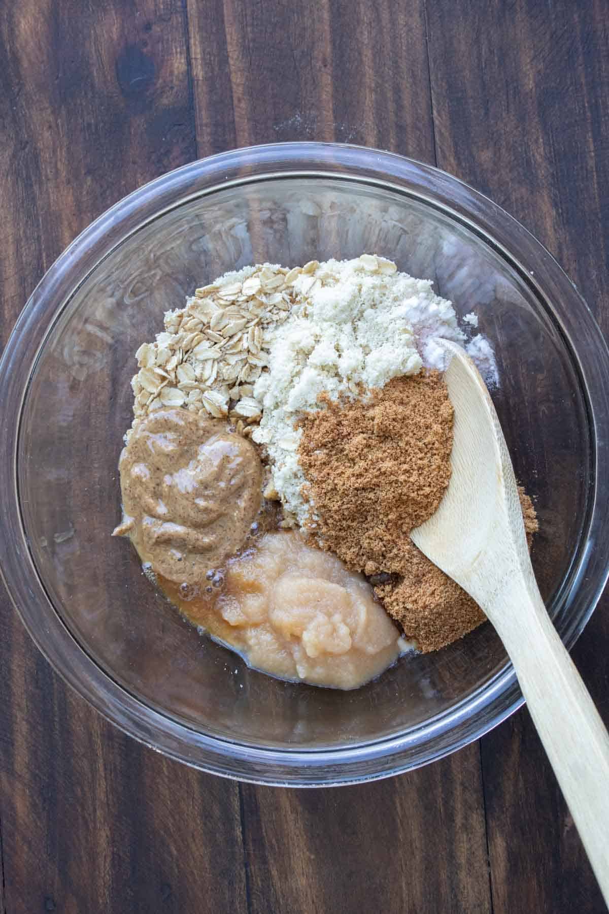 Wooden spoon mixing ingredients for oatmeal cookies in a glass bowl