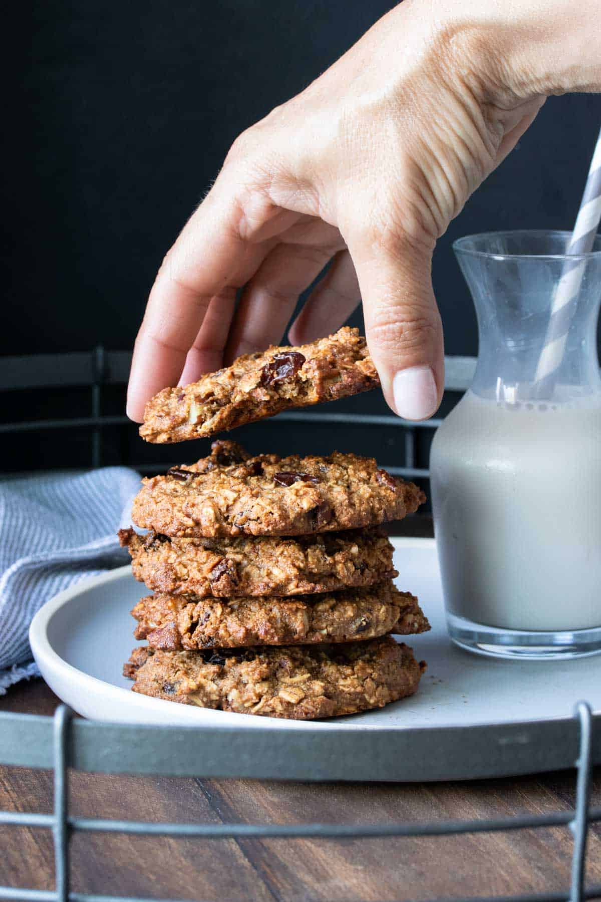 Hand grabbing the top oatmeal raisin cookie from a stack