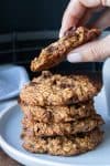 Hand holding a half eaten oatmeal raisin cookie over a stack of more