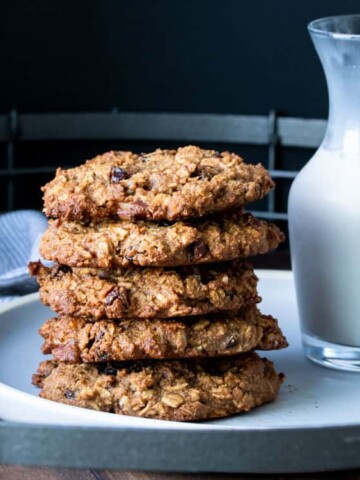 Five oatmeal raising cookies stacked on a plate next to a glass of milk