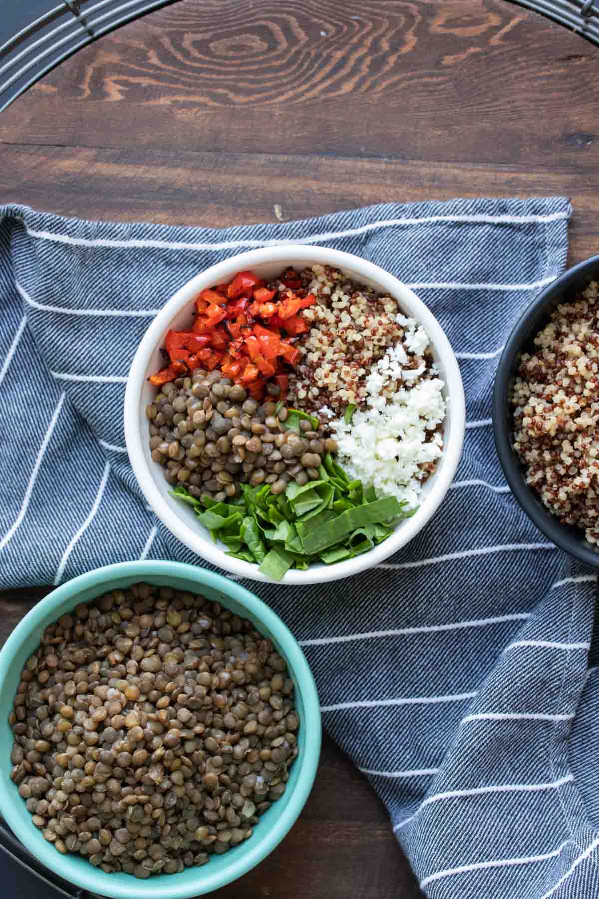 Bowls of lentil quinoa salad ingredients on a blue striped towel