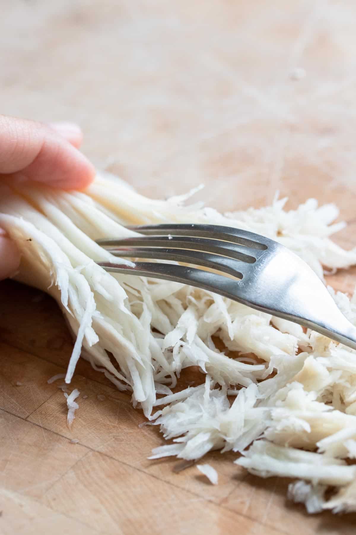 Fork shredding a mushroom on a wooden surface