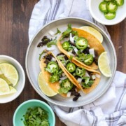 Grey plate with three carnitas tacos on it topped with jalapeños