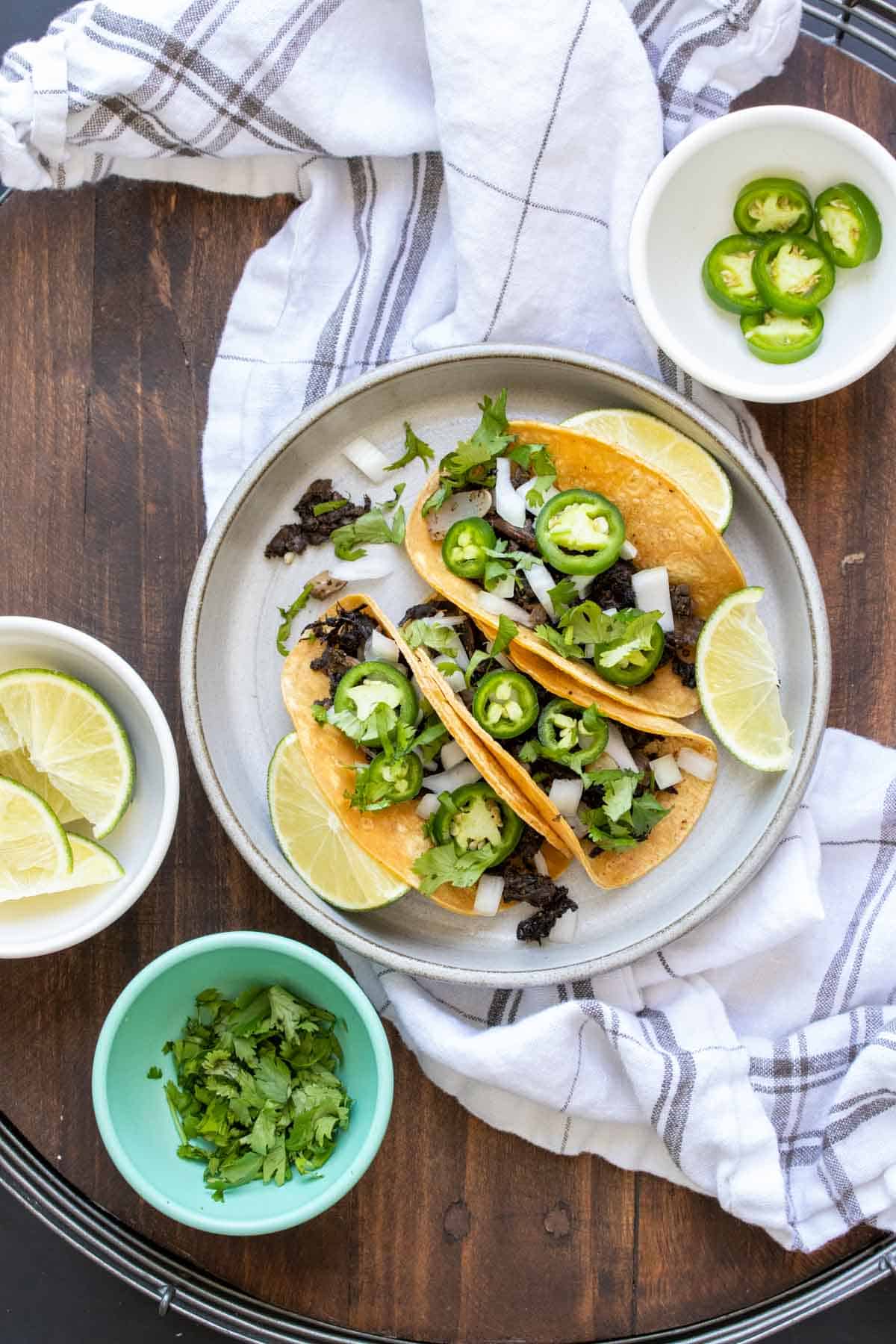 Grey plate with three carnitas tacos on it topped with jalapeños