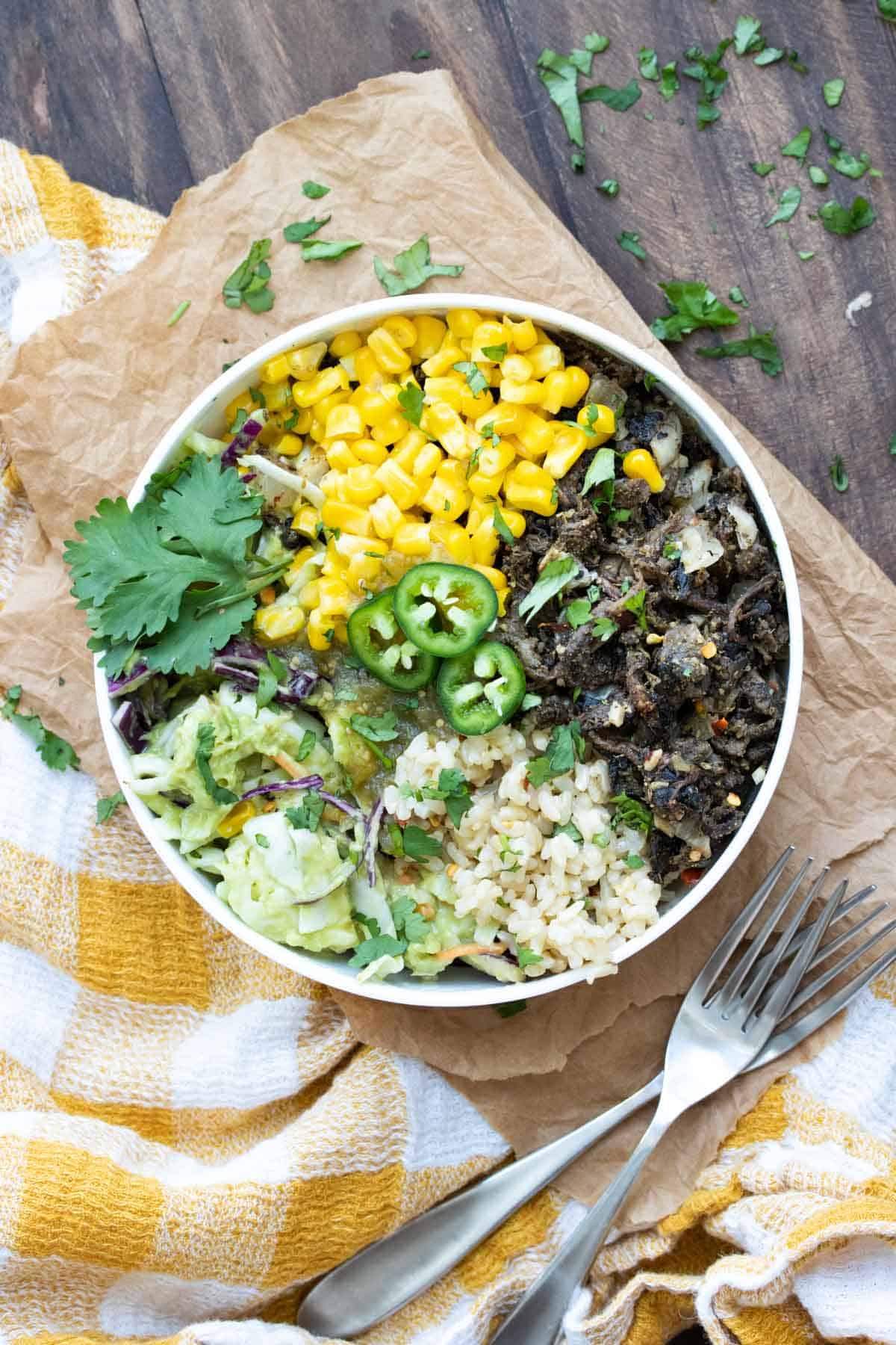 Shredded mushroom carnitas, cabbage salad, brown rice and corn in a white bowl