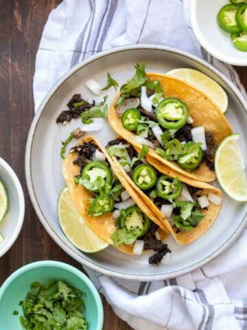 Grey plate with loaded carnitas tacos surrounded by bowls of ingredients