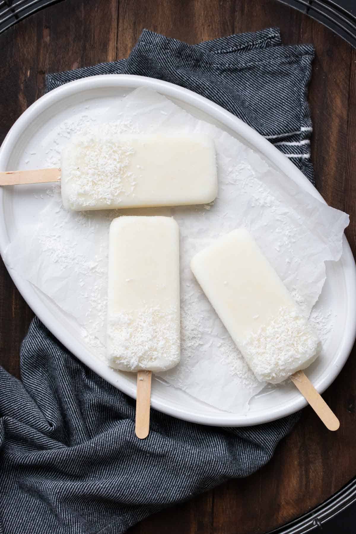 White popsicles with shredded coconut covering the bottom half on a white plate