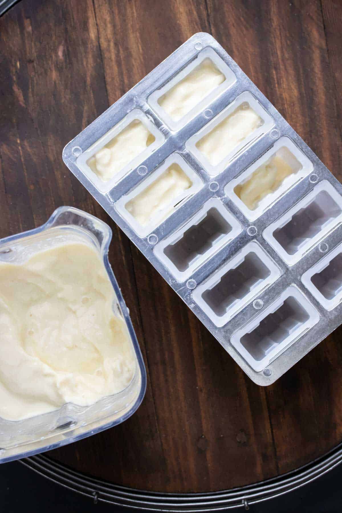 Top view of a blender with pina colada popsicle mix next to popsicle molds