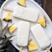 White platter of creamy looking popsicles next to pieces of pineapple