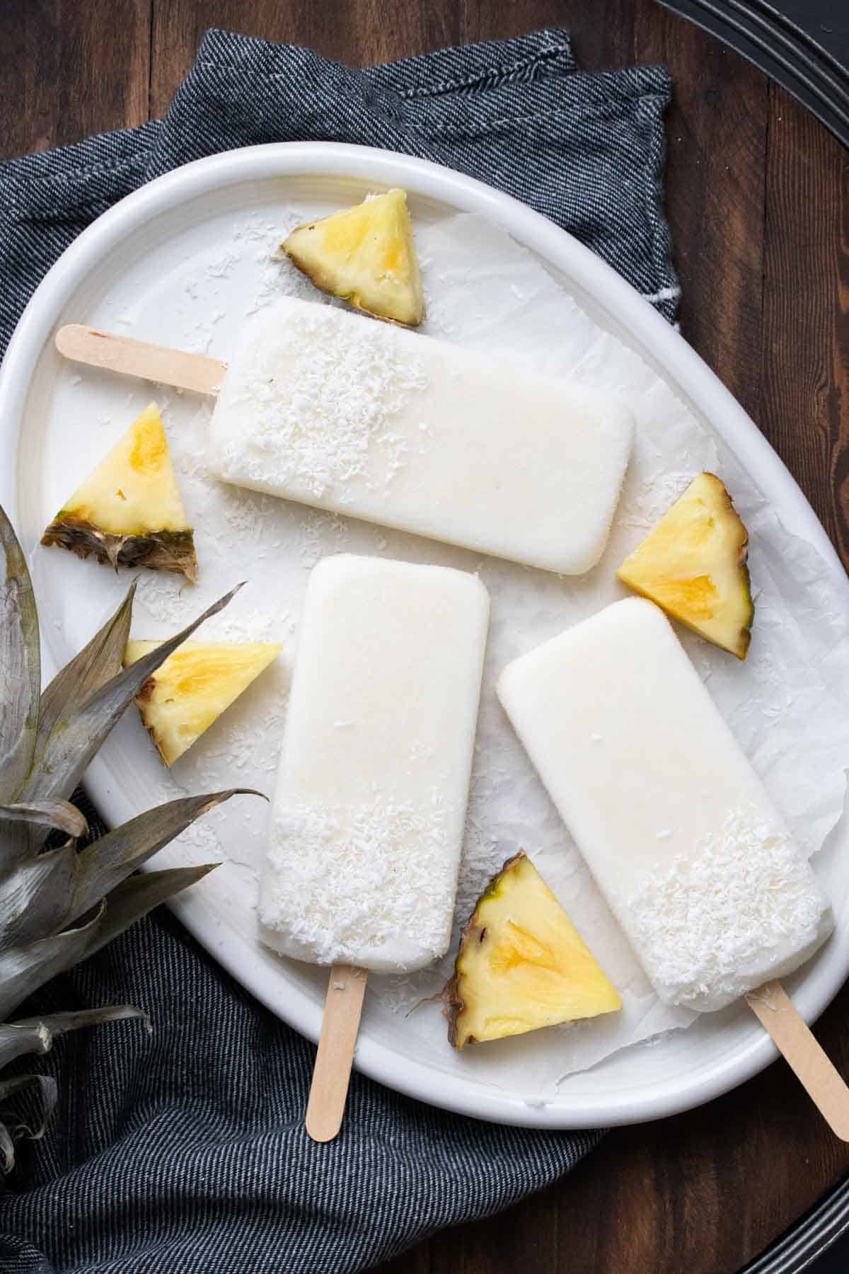 White platter of creamy looking popsicles next to pieces of pineapple