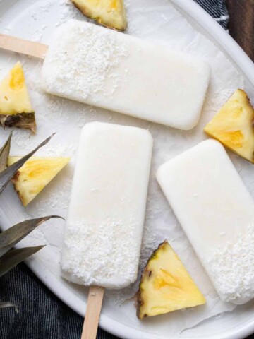 White plate with pina colada popsicles next to pieces of pineapple