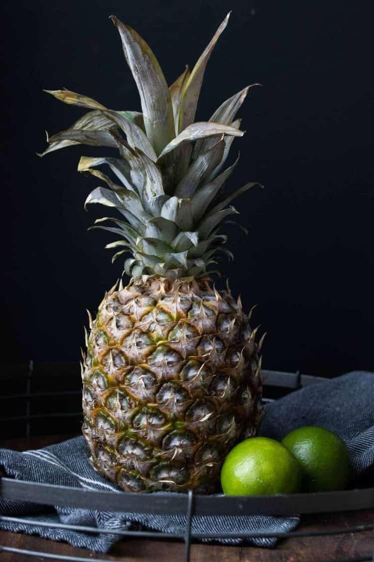 A pineapple next to 2 limes on a blue kitchen napkin