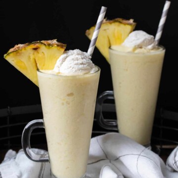 Two pina colada smoothies with whipped cream and a pineapple slice