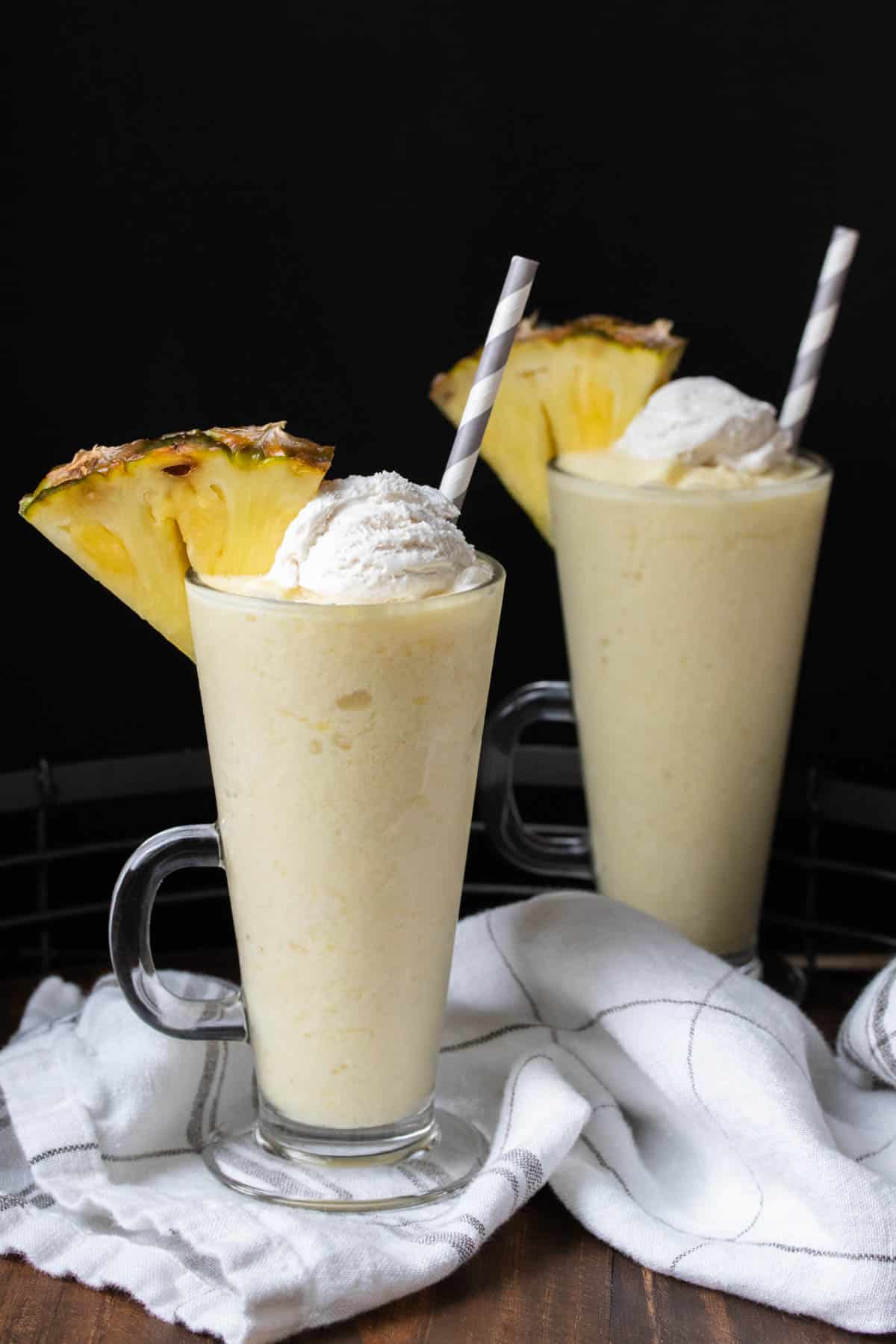 Two pina colada smoothies with whipped cream and a pineapple slice