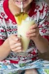 A child holding a pine colada smoothie in a tall glass jar