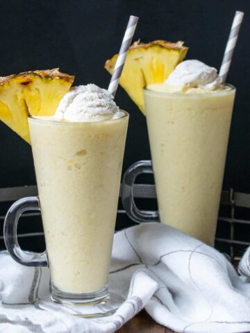 Front view of two glass jars filled with pina colada smoothies and a pineapple slice