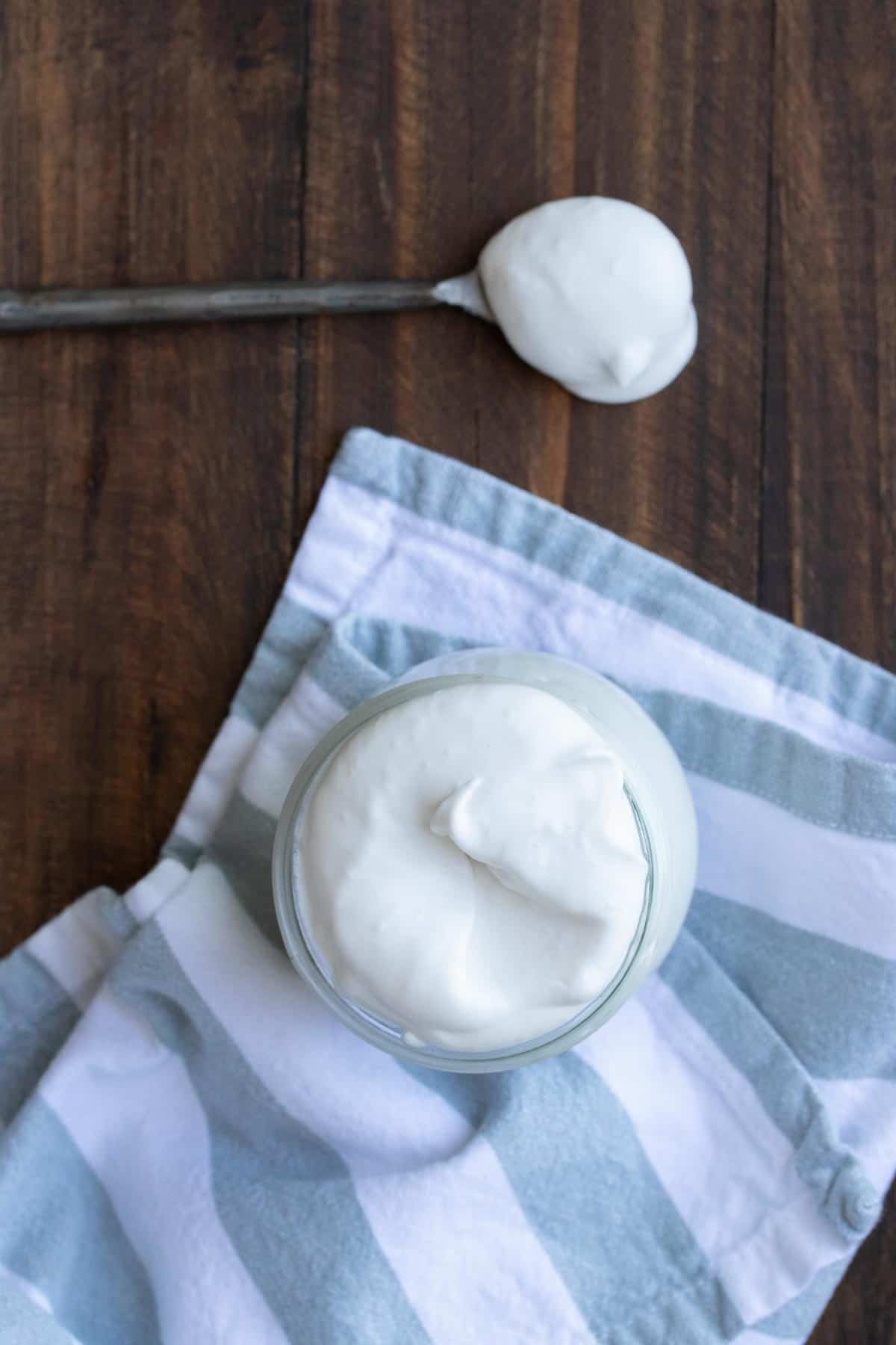 Top view of a glass jar with vegan whipped cream next to a spoonful of it.