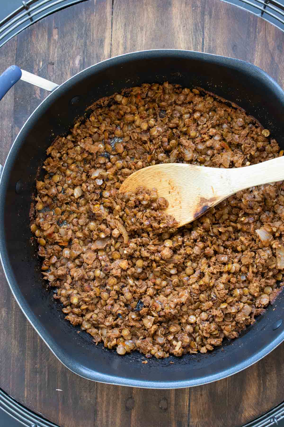 Cooked lentil and walnut being mixed around in a pan with a wooden spoon