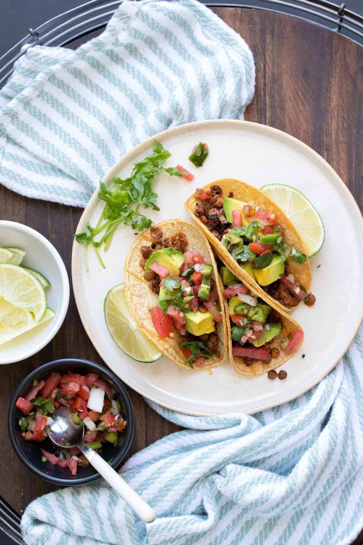 White plate with tacos filled with lentil taco meat and toppings.