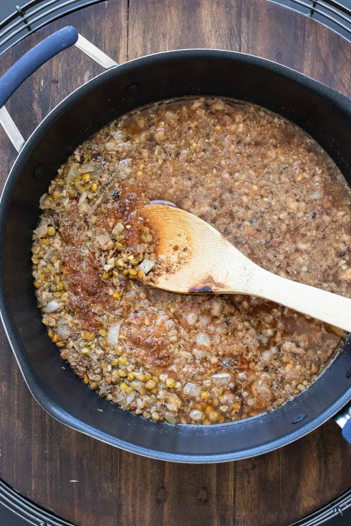 Wooden spoon mixing a bean and broth mixture in a pan