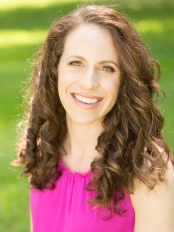 Woman with curly hair wearing pink shirt smiling at the camera