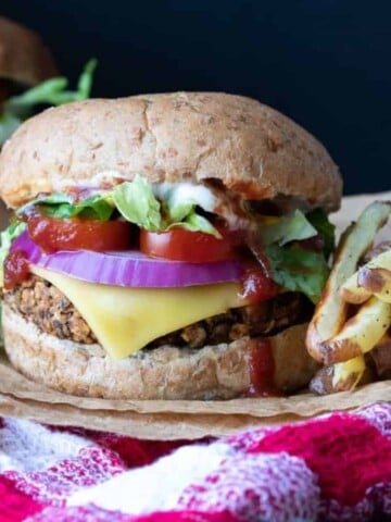 A burger with cheese, onion, lettuce and tomato on a red checkered towel