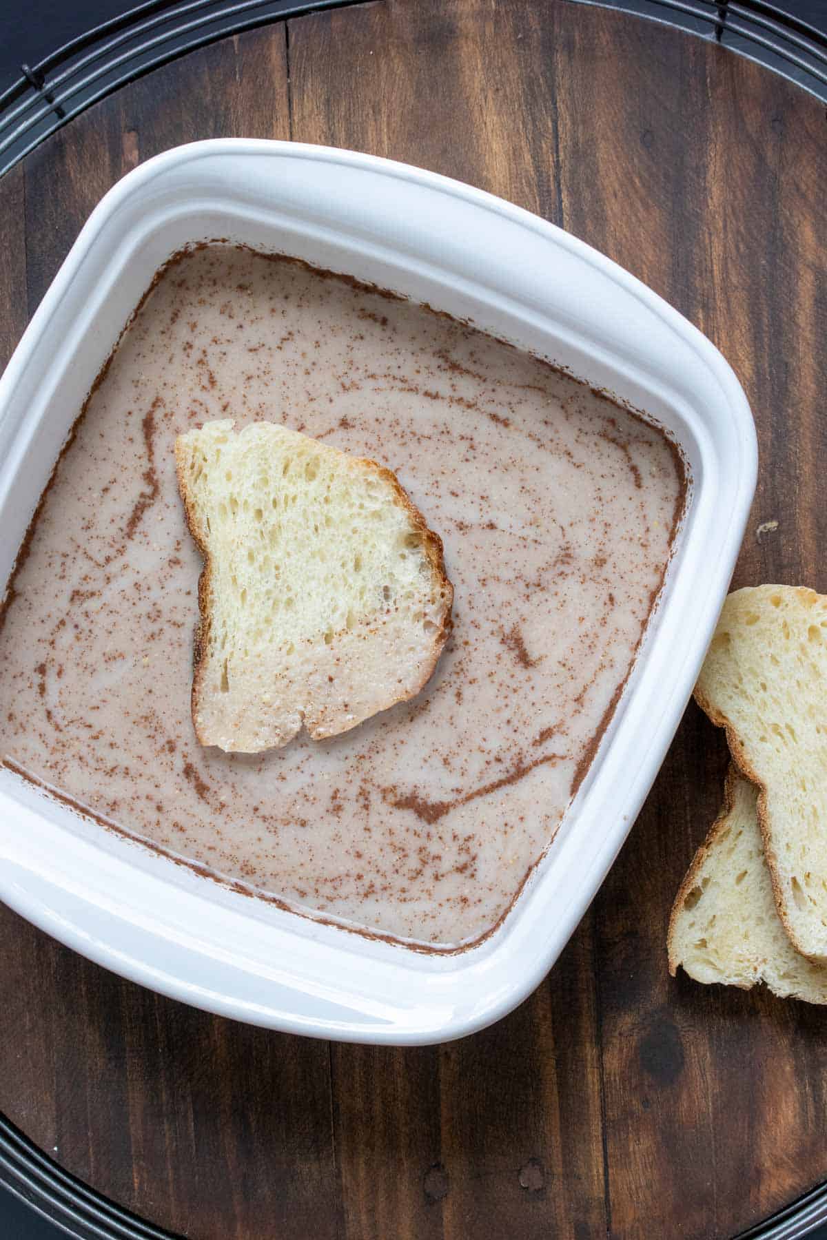 A piece of bread in a white pan filled with brownish milky liquid