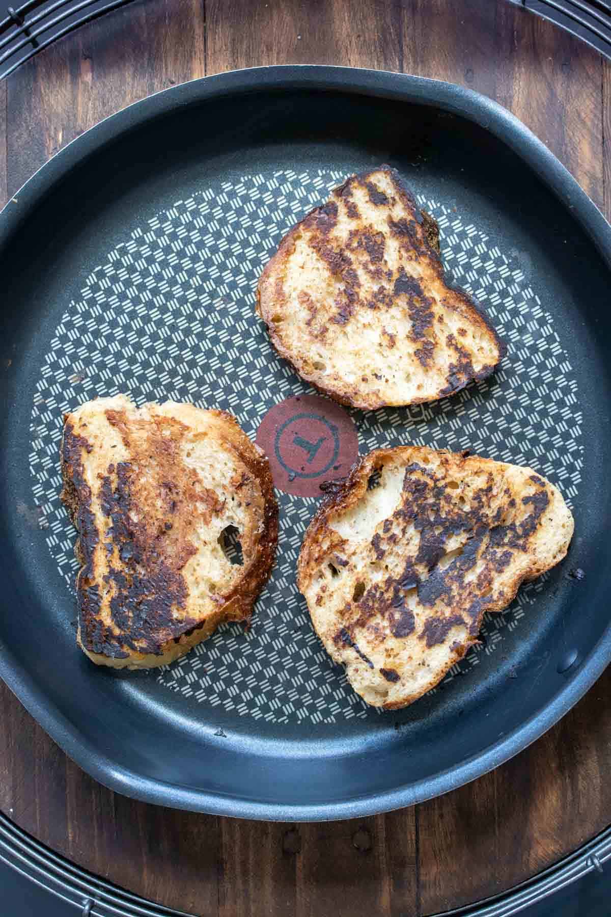 Three pieces of French toast being grilled on a black pan.