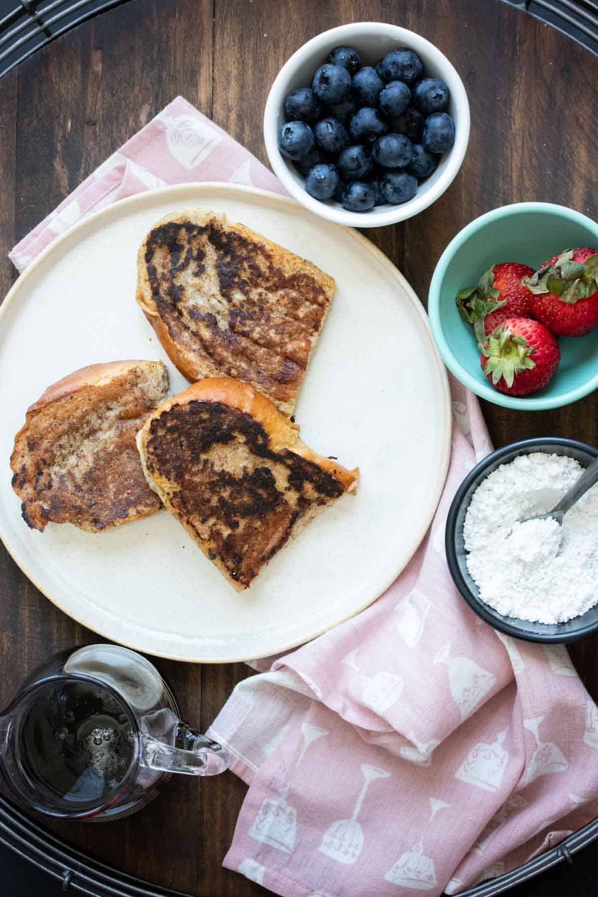 Three pieces of dry French toast on a cream plate with bowls of toppings