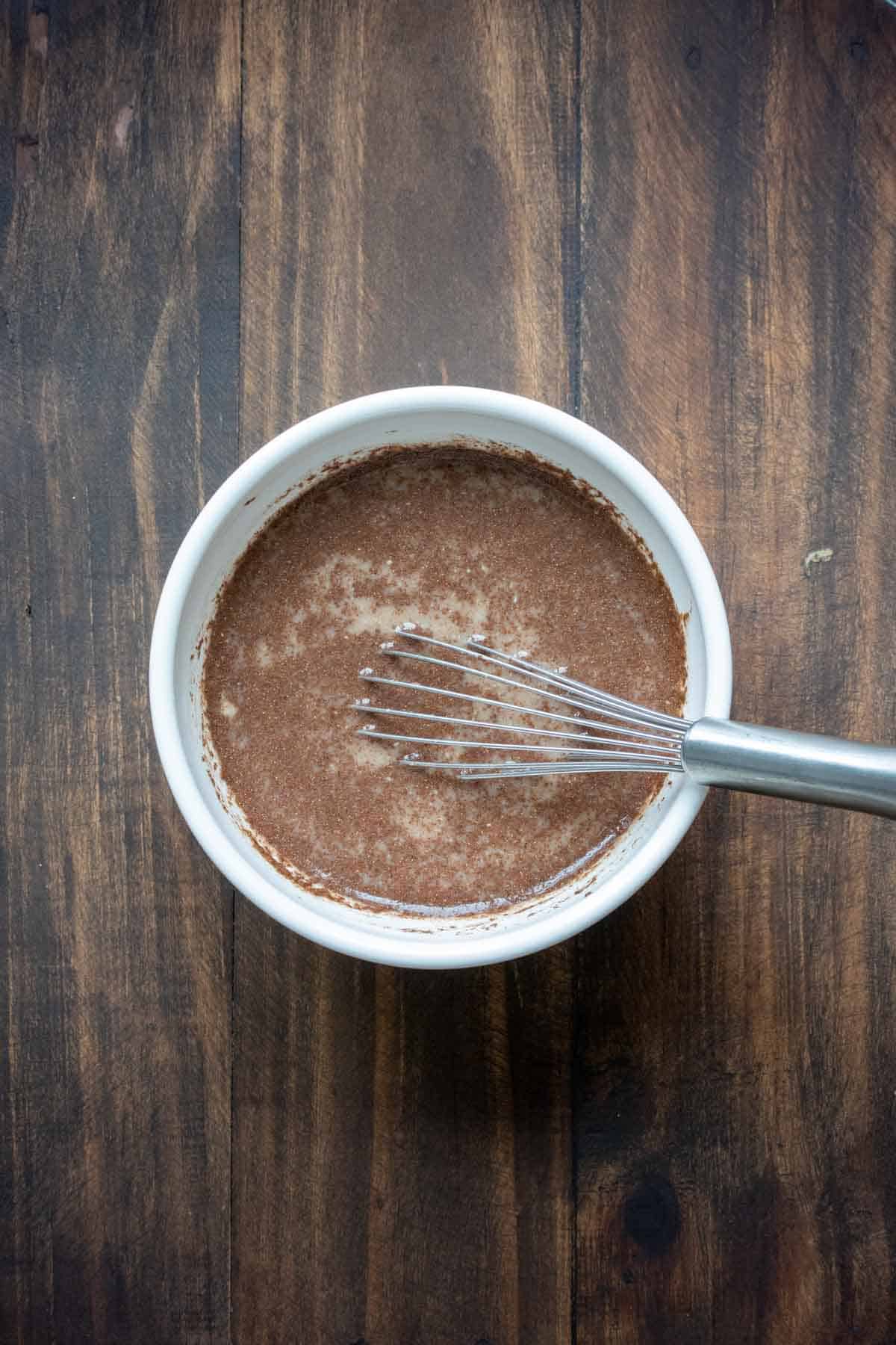 Whisk mixed a milky brownish liquid in a white bowl.