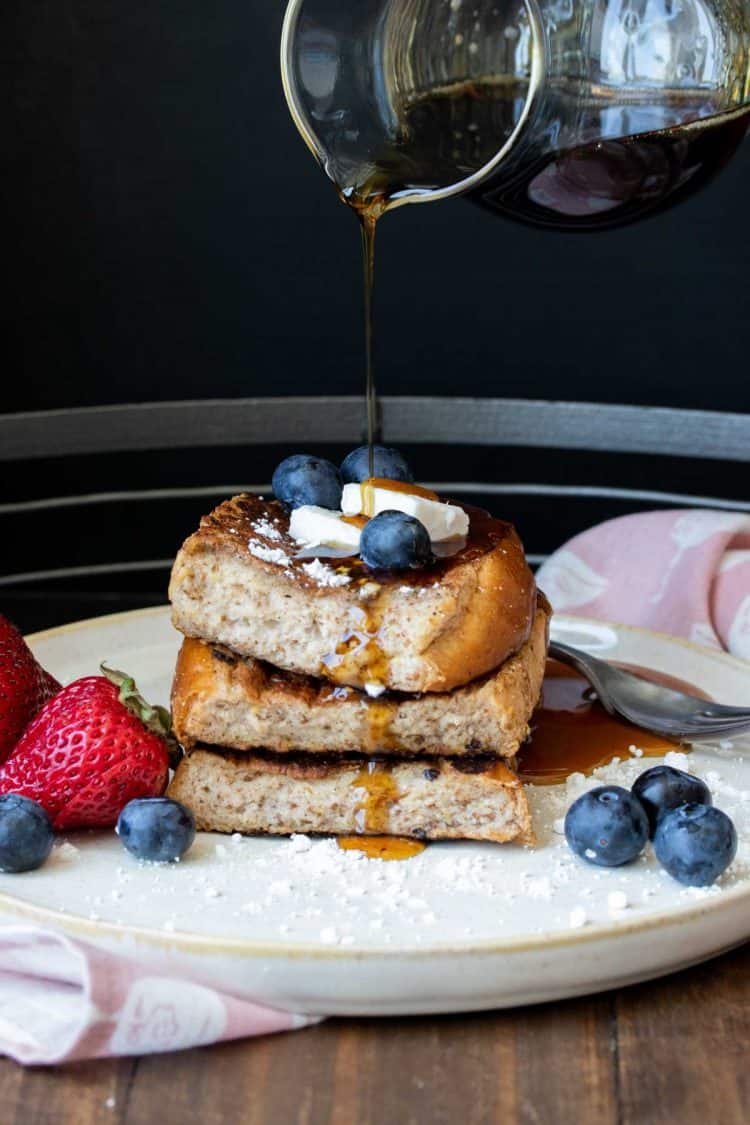 Maple syrup being poured onto a pile of French toast and berries