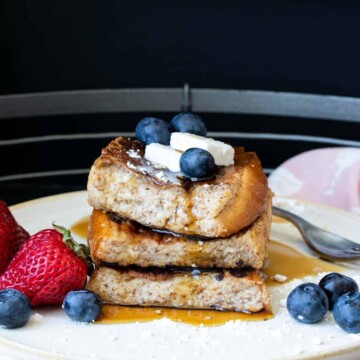 Three pieces of French toast topped with butter and berries piled up