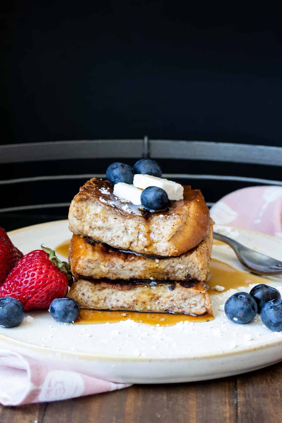 Three pieces of French toast topped with butter and berries piled up